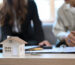 House model on wooden table and  financial adviser consulting contract mortgage loan with elderly man in background.