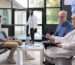 Senior doctor standing beside elderly patient discussing health care treatment during checkup visit appointment in hospital waiting area. Old man filling insurance report before start consultation